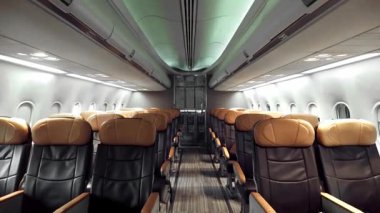 Deri koltukları ve çevre aydınlatması olan boş bir modern uçak kabininin geniş açılı görüntüsü, ticari havayolu oturma düzenini, iç tasarımı, rahatlığı ve seyahat hazırlığını gösteriyor.