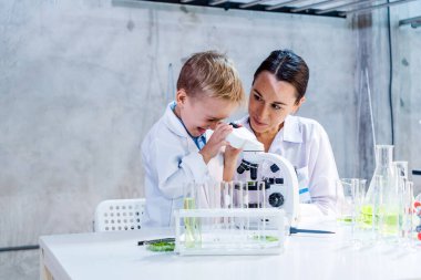 Genç bir erkek ve dişi bilim adamı mikroskop altında bitki örneklerini inceleyerek çevre dostu tarım teknolojisini öğreniyor. STEM eğitimini, sürdürülebilirliği, tarımda yeniliği teşvik eder.