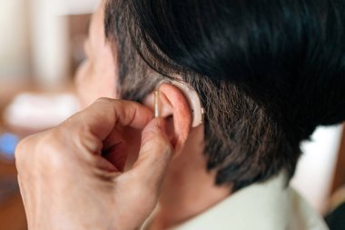 İşitme cihazını ayarlayan, sağlık desteği gösteren, asist işitme teknolojisi kullanan ve işitme engelli bireyler için günlük bağımsızlık çözümleri sunan üst düzey bir kadının yakın çekimi.