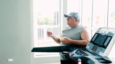 Meyve yerken koşu bandında yürüyen şişman bir adam, aktif yaşlanma, sağlıklı yaşam tarzı ve sağlıklılığı teşvik ediyor. Fitness motivasyonu, kilo kaybı ve yaşlılar için dengeli yaşam kavramı.