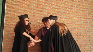 Mutlu genç mezunlar mezuniyet töreninden sonra sevinç ve dostluk göstererek alkış ve alkış ile kutluyorlar. Başarı anı tuğla duvarın arkasında yakalanır..