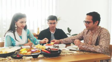 Çeşitli Hint ailesi geleneksel giysiler giyerek ve otantik yiyecekleri paylaşarak birlikte ziyafet çekiyorlar. Kutlama, kültür ve birliktelik. Parlak, neşeli bir yemek masasında..