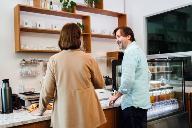 Kafe sahibi, modern bir kahve dükkanında danışman ile finansal planlamayı tartışıyor. Rahat ve profesyonel bir ortamda küçük işletme işbirliği, yatırım danışmanlığı ve takım çalışması.