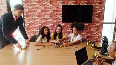 Öğrenciler, eğitmenlerin rehberliğinde bir kodlama sınıfında robotik bir araç oluşturarak birlikte çalışıyorlar. Derste BTMM eğitimi, yaratıcılık ve gelecekteki teknoloji öğrenme deneyimleri ele alınıyor.