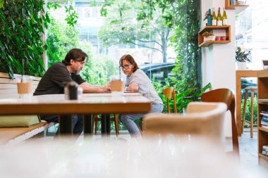 Kafe sahibi ve finans danışmanı parlak bir kafe ortamında fikirlerini gülücüklerle paylaşıyorlar. Dizüstü bilgisayardaki planları gözden geçirirler, pozitif işbirliğini, küçük işletme desteğini ve finansal büyümeyi sembolize ederler..