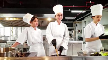 Aşçı eğitmeni ve üniformalı öğrenciler ticari bir mutfakta yeni pişirilmiş makarna. Sahnede takım çalışması ve elle öğrenme, aşçılık okulu veya yemek hazırlama kavramları için ideal.