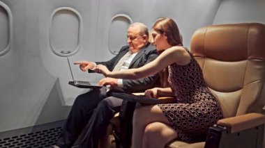 Uçuş sırasında laptopta işbirliği yapan iki iş yolcusu. Kablosuz internet kavramı, verimlilik, şirket seyahati, modern havayolu hizmetleri, rahat koltuklar. Yavaş çekim 4k video