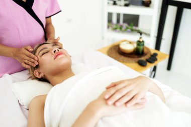 Kadın, beyaz bir havluya sarılı modern bir kaplıcada rahatlatıcı bir yüz masajı yaptırıyor. Sakin ve gençleştirici bir ortamda sağlık, güzellik terapisi, cilt bakımı ve kaplıca hizmetlerini ön plana çıkarır.