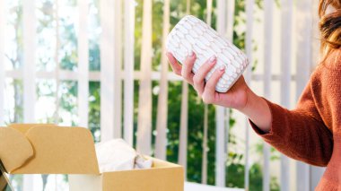 Açık bir nakliye kutusundan geometrik desenli beyaz ahşap bir vazoyu inceleyen bir kadın. Çevrimiçi alışveriş, boks yapma, ürün kalitesi kontrolü ve evde müşteri deneyimi kavramı.