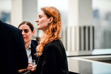 Kendine güvenen iş kadını, iş arkadaşlarıyla çatıdaki bir toplantıda sakin bir anın tadını çıkarıyor. Profesyonellerin açık hava kurumsal atmosferde gevşeyip bağlandıkları sıradan bir iş sonrası etkinliği..