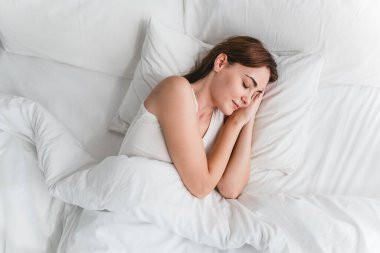 Beyaz bir yatakta yatan genç bir kadın, kadınların zihinsel berraklığı, duygusal dengesi ve huzur verici bir çevrede fiziksel sağlığı için kalitenin önemini gösteriyor.