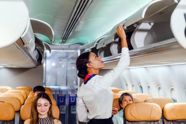 Uçuş görevlisi, modern bir uçak kabininde, yolcuların oturduğu koltukları emniyete alıyor..