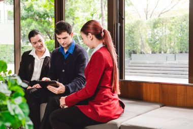 Üç iş arkadaşı, tablet stratejisini tartışmak için modern ofis salonunda işbirliği yapıyorlar. Resmi olmayan toplantıda takım çalışması, danışma, planlama ve başlangıç odaklı tartışma vurgulandı.