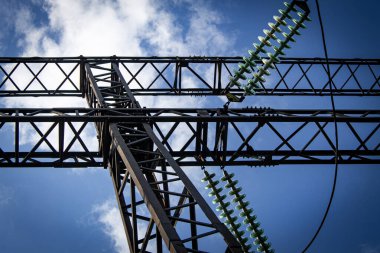 Güneşli bir yaz gününde mavi gökyüzüne karşı izolatörlerle yüksek voltajlı elektrik hattının metal desteği.