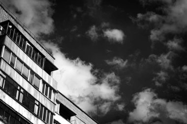 Beyaz bulutlu mavi gökyüzünün arka planına karşı çok katlı tuğla binanın son katları. Şehir çizimleri, taş ormanları. Siyah beyaz fotoğraf