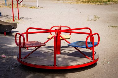 Renkli yatay fotoğraf, oyun parkında kırmızı atlıkarınca, güneşli bir günde kumdan bir arka plan, şehir manzarası.