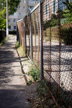 Renkli dikey fotoğraf, metal tel örgü çitleri, kentsel sokak ve konut arka planlı.