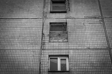 Tek renkli yatay fotoğraf, kahverengi kiremitli ön cephesi olan eski bir iskan binası, pencereler tek sıra halinde, tepeden tırnağa odaklanmış..