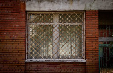 Renkli yatay fotoğraf, camlarında metal parmaklıklar olan tuğla kırmızı bina ve ahşap çerçeveler, şehir arka planı..