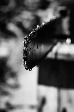 Elektrikli testere zincirinin dikey yakın plan fotoğrafı. Güneşli bir yaz gününde arka planda bulanık bir şekilde bahçede çalışırken bir el aleti. Nesnenin yan görünümü.