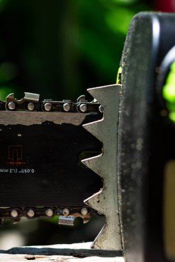 Renkli dikey fotoğraf, zincir ve elektrikli testerenin yakın çekimi, güneşli yaz gününde bahçe işleri sırasında el aleti ve bulanık arka plan..