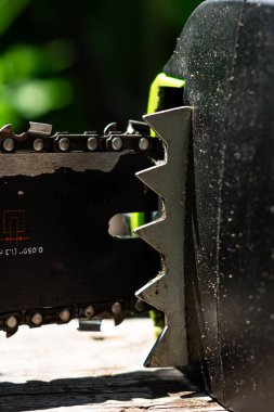 Renkli dikey fotoğraf, zincir ve elektrikli testerenin yakın çekimi, güneşli yaz gününde bahçe işleri sırasında el aleti ve bulanık arka plan..