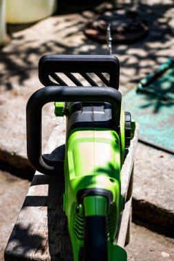 Elektrikli testerenin, güneşli bir yaz gününde arka planı bulanık bir şekilde bahçıvanlık yapmak için kullanılan elektrikli testerenin dikey renkli fotoğrafı. Nesnenin üst görünümü.