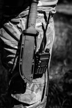 Askeri bir bıçak ve telsiz üniformalı bir askerin kemerinde asılı. Askeri teçhizat, taktik teçhizat, savaş operasyonları için teçhizat. Siyah beyaz fotoğraf