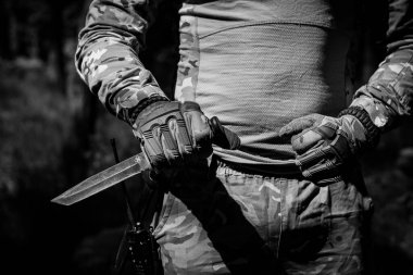 Bir askeri bıçak ve onu tutan taktik eldivenli bir el. Askeri işler, taktik ekipmanlar. Siyah beyaz fotoğraf