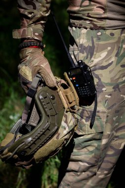 Taktik eldivenli bir asker elinde telsiz, askeri mühimmat, kamuflaj ve askeri işler olan bir saldırı kaskı tutuyor. Askeri üniforma.
