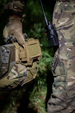 Taktik eldivenli bir asker elinde telsiz, askeri mühimmat, kamuflaj ve askeri işler olan bir saldırı kaskı tutuyor. Askeri üniforma.