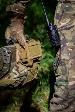 Taktik eldivenli bir asker elinde telsiz, askeri mühimmat, kamuflaj ve askeri işler olan bir saldırı kaskı tutuyor. Askeri üniforma.