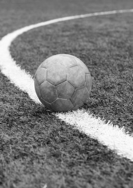 Yeşil bir futbol sahasına yakın eski kirli bir topun tek renkli dikey fotoğrafı. Takım sporu, stadyumda futbol maçı..