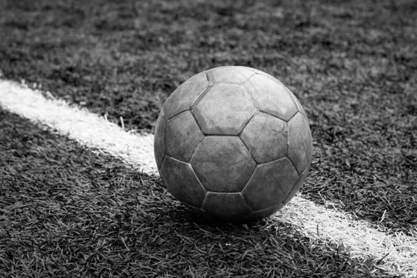 Yeşil bir futbol sahasında eski kirli bir topun tek renkli yatay fotoğrafı. Takım sporu, stadyumda şehir planlı futbol maçı..