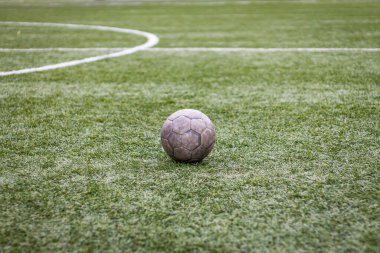 Renkli yatay fotoğraf, yeşil çimlerde eski futbol topu ve beyaz çizgi, stadyumda aktif spor. 