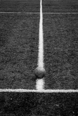 Tek renkli dikey fotoğraf, yeşil çimenli ve beyaz çizgili eski futbol topu, stadyumda aktif spor. 