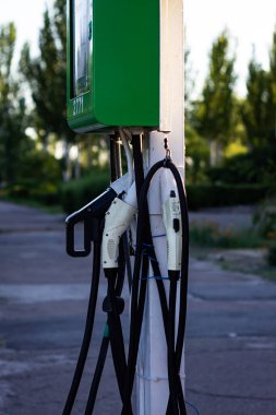 Renkli dikey fotoğraf, elektrikli arabalar için elektrik şarj istasyonu güneşli bir günde açık hava, şehir manzarası..