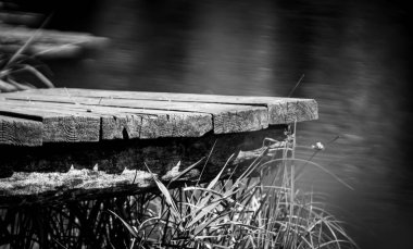 Ahşap platform, kısmen yemyeşil yeşillikler ve uzun otlarla gizlenmiş sakin bir nehrin üzerine uzanır.. 