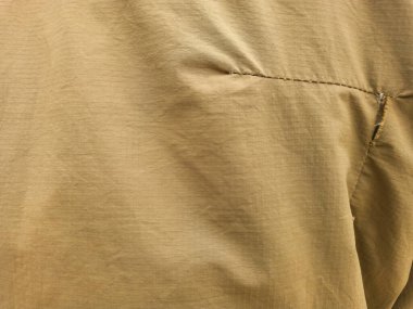 Görüntü üzerinde yatay olarak uzanan görünür dikişleri olan, biraz buruşuk, kahverengi bir kumaş görüntüsü..