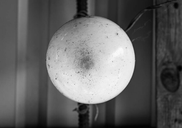 Совершенно сферический, бледно-белый шар висит на виселице, его тонкие текстуры контрастируют с размытым, промышленным фоном из гофрированного металла и теплого дерева.