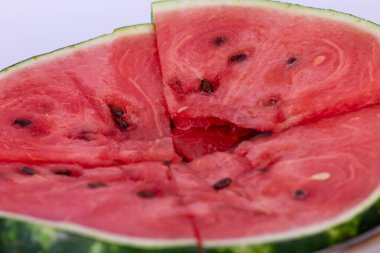 Dört sulu karpuz dilimi parlak kırmızı etleri ve dağınık siyah tohumlarıyla bir daire şeklinde dizilir. Doku sulu ve nemli, olgun bir karpuzun tipik dokusu..
