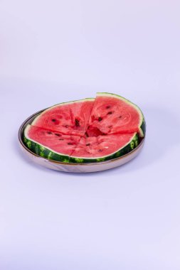 Bir tabağa dizilmiş karpuz dilimleri. Meyvenin koyu yeşil çizgili deriyle çelişen siyah çekirdekli parlak kırmızı bir merkezi vardır. Dilimler düzgünce yerleştirilmiş..