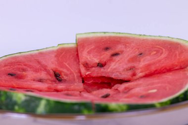 Dilimlerin doğal eğrisi, meyvenin taze ve çekici görünümünü vurgulayarak neredeyse tam bir daire oluşturur. Deri kısmen görülebilir, kırmızı iç kısımla çelişiyor..