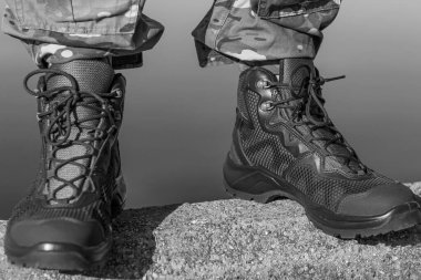 Bir askerin taktik botlar ve kamuflaj pantolonu giymiş, taş bir yüzeye sıkıca yerleştirilmiş tek renkli ayakları. Dayanıklılık ve görevi temsil eder..