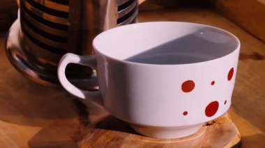 Tahta tepside duran cam bir çaydanlıktan fincana kahve dolduran bir kadının yakın çekimi..