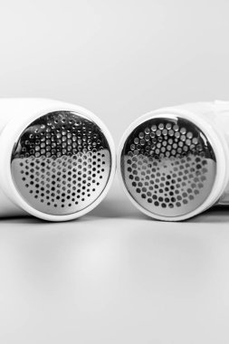 Metalik tıraş ekranlarına odaklanmış iki elektrikli kumaş traş makinesinin monokrom yakın çekimi. Giysilerinizi yenilemek ve hapları çıkarmak için gerekli araçlar.