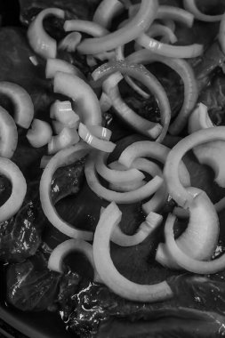 Yoğun siyah beyaz et, muhtemelen sığır eti ya da karaciğer, bol bol kalın, taze soğan halkalarıyla kaplanmış, marine edilmeden önce dokudaki kontrastı vurguluyor..