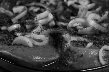 Tek renkli çiğ domuz bifteği. Kuru otlar ve baharatlarla bol baharatlı. Taze soğan halkalarıyla süslenmiş ve lezzetli bir yemeğe hazır..