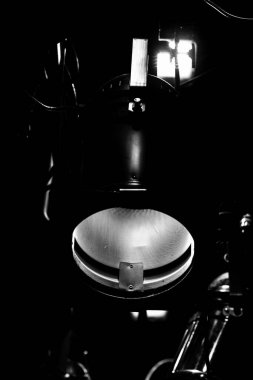 Tiyatro sahnesinin dramatik bir siyah-beyaz yakın çekimi. Yüksek kontrast, derin gölgelerden ortaya çıkan metalik dokuyu ve teknik ayrıntıları vurgular..