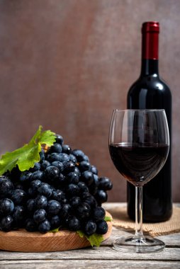 Şarap şişesi ve kırmızı şarap kadehi ve ahşap masada taze üzümler. Seçici odak.